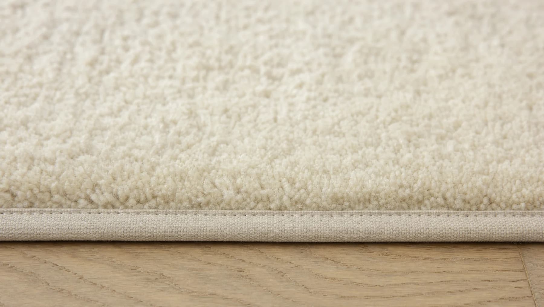Cut-pile carpet with a cotton bound edge, shown where it meets a wood floor