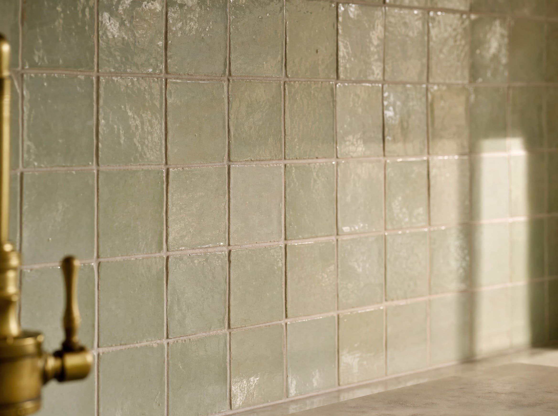 Handmade glazed zellige backsplash in a soft sage glaze catching warm light — representative rendering