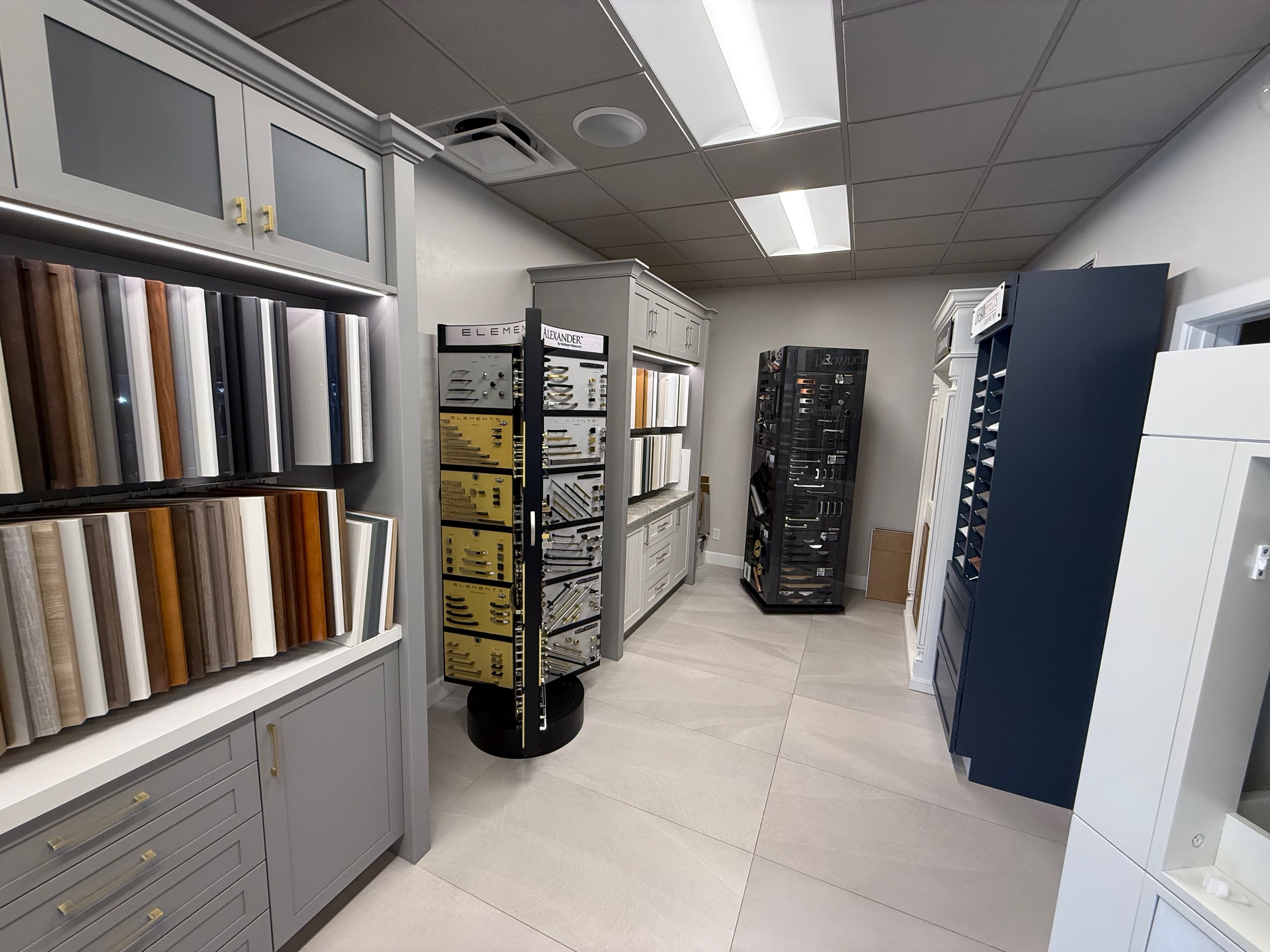 The door and finish wall in the ProFloors Naples showroom — dozens of cabinet door faces racked on edge beside the Elements and Alexander hardware spinners