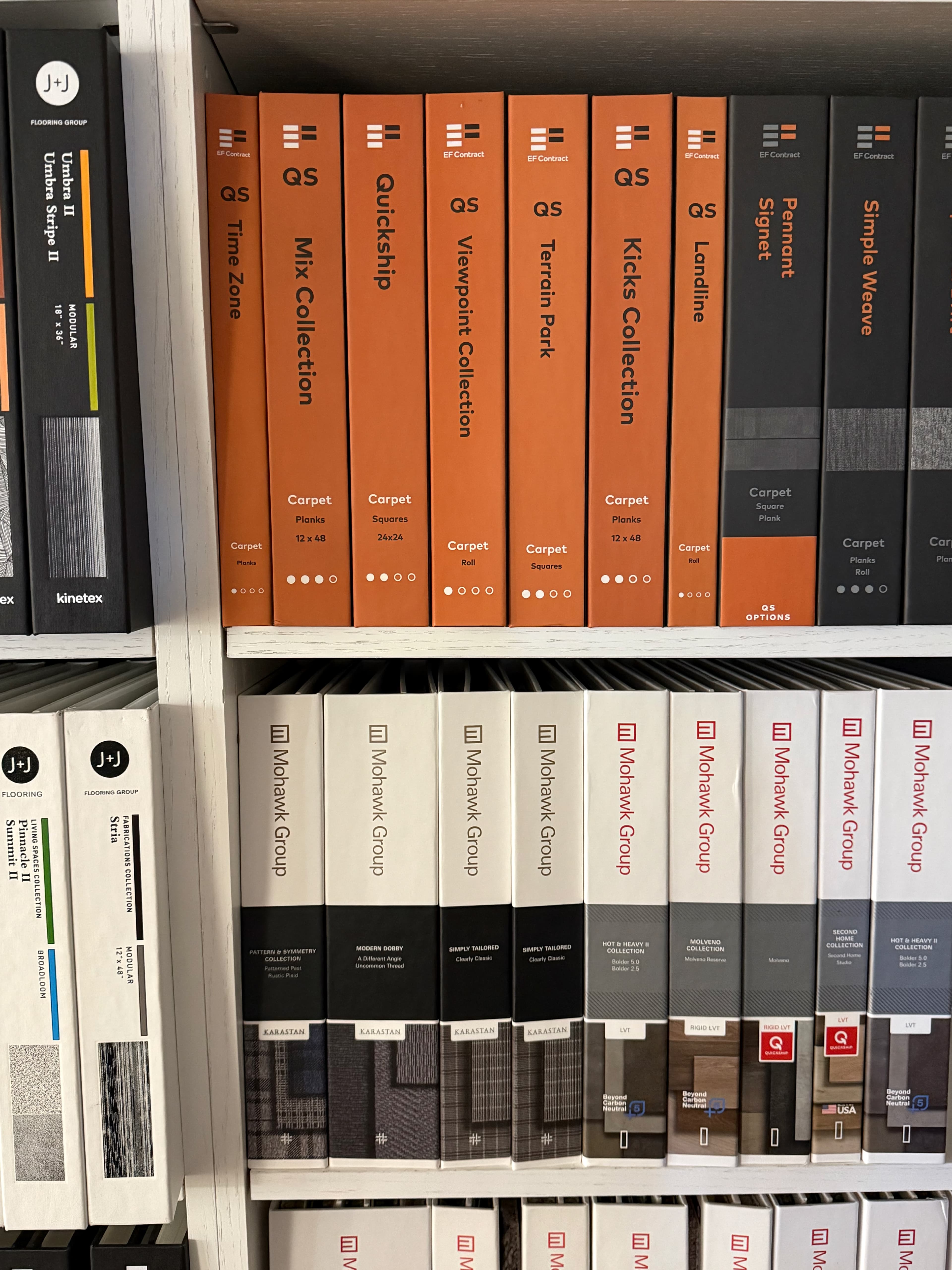 Carpet sample binders shelved at the ProFloors Naples showroom — J+J Flooring Group, EF Contract Quickship, and Mohawk Group Karastan collections.