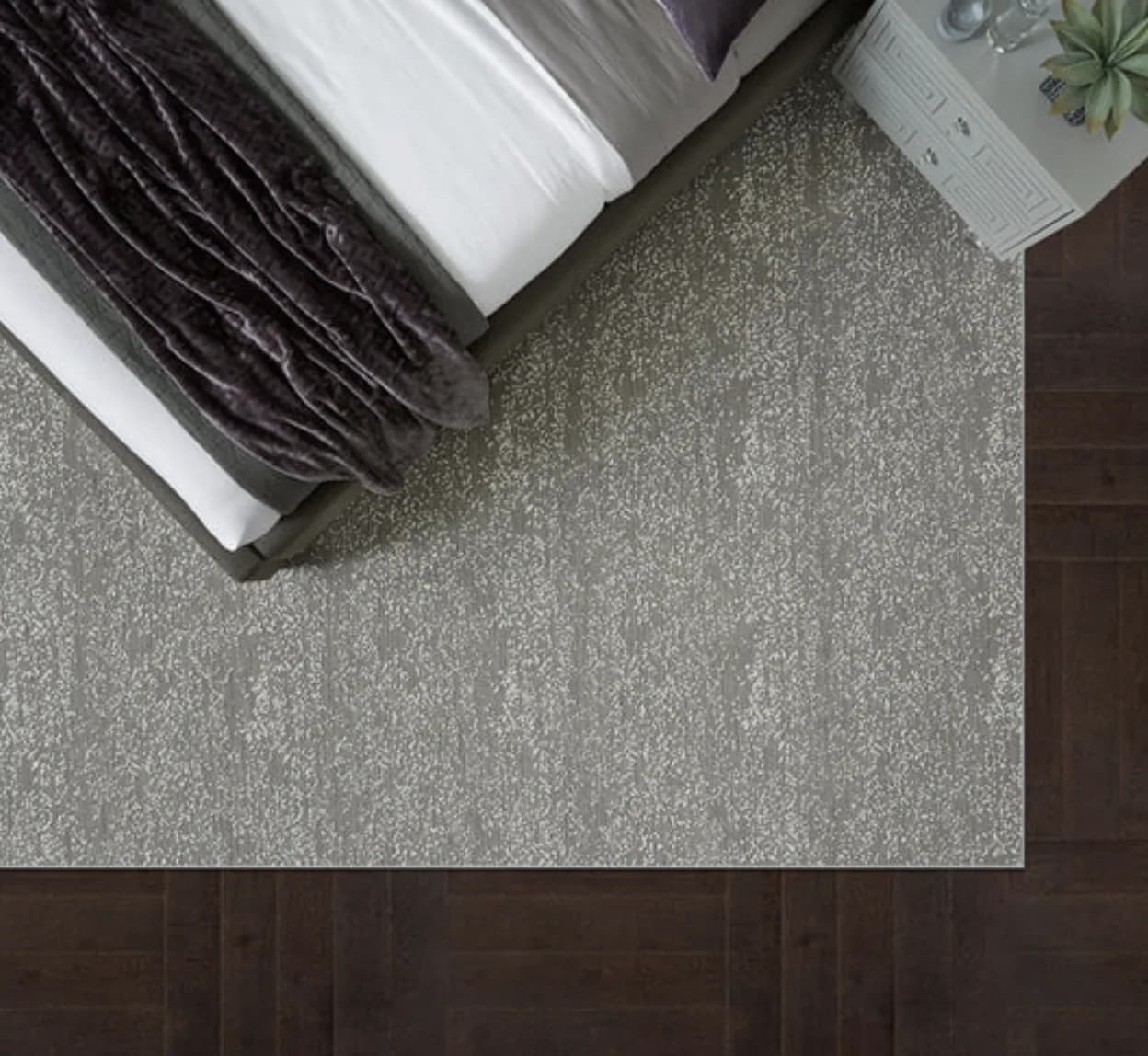 A hand-bound custom rug edge laid over a finished dark-wood floor beside a bed in a Naples home