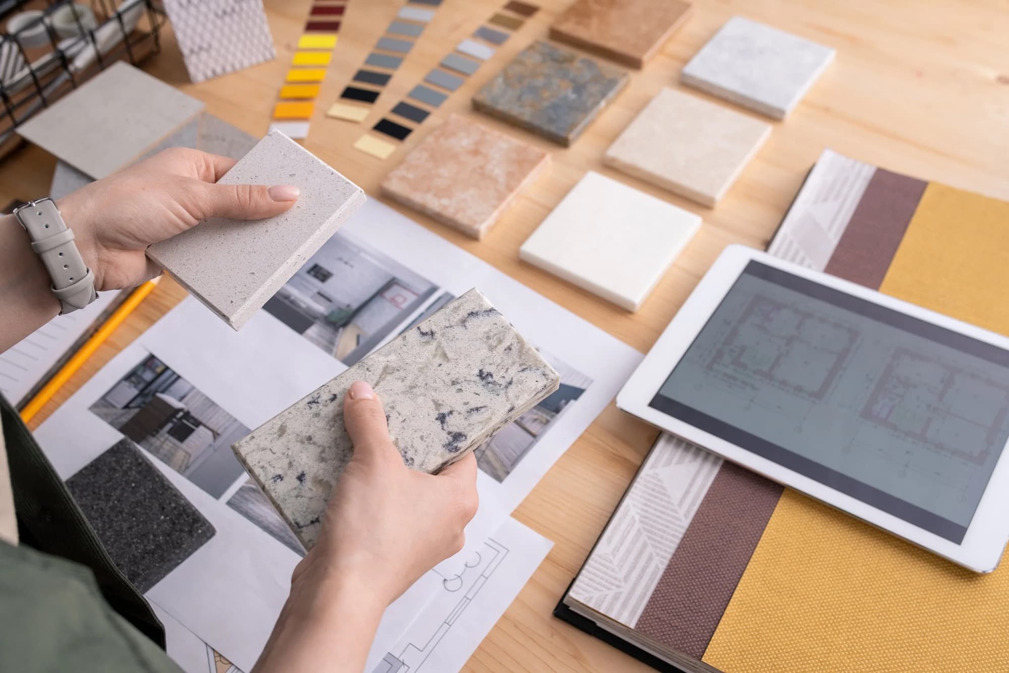 Hands comparing stone and tile samples over a floor plan while planning a flooring job.