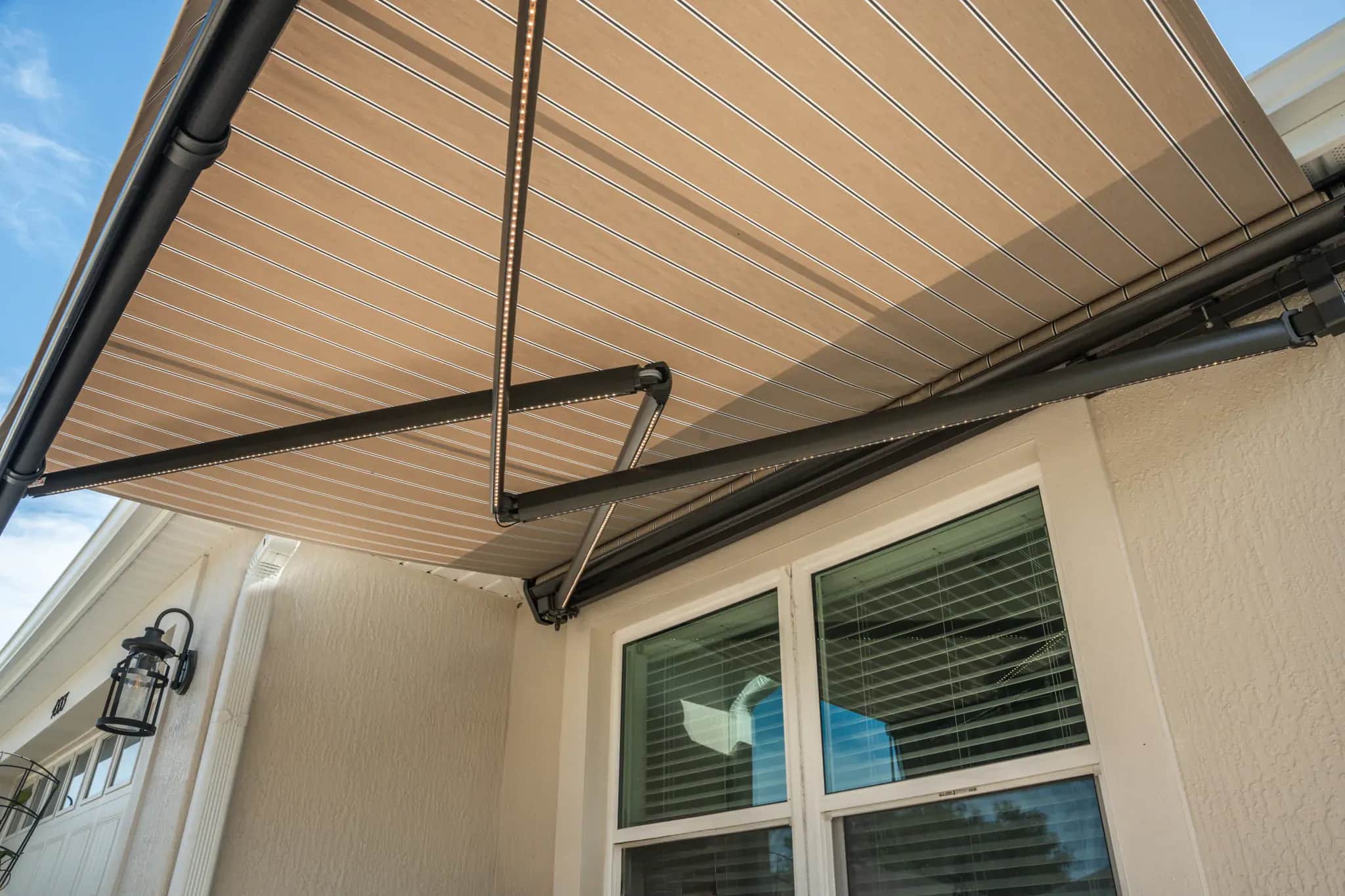 Underside of a striped SunPro awning showing its fabric, crossarms, housing, and lighting